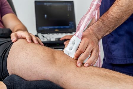 eco Close-up of a physiotherapist performing an ultrasound of the knee on a patient lying on the stretcher